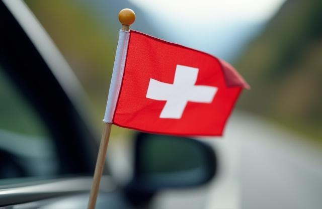 Small Swiss flag waving near a car on a road.